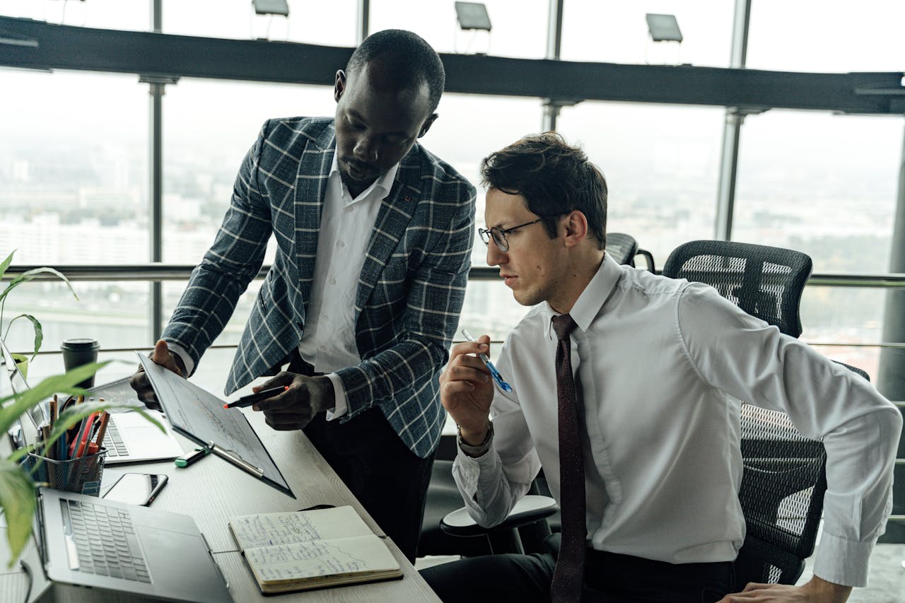 Services Two businessmen collaborate in a modern office setting, engaged in a focused discussion.